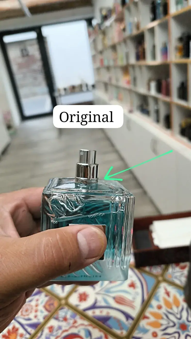 Cuello metálico del atomizador asentado sobre el vidrio de un frasco azul, señalado como montaje de referencia